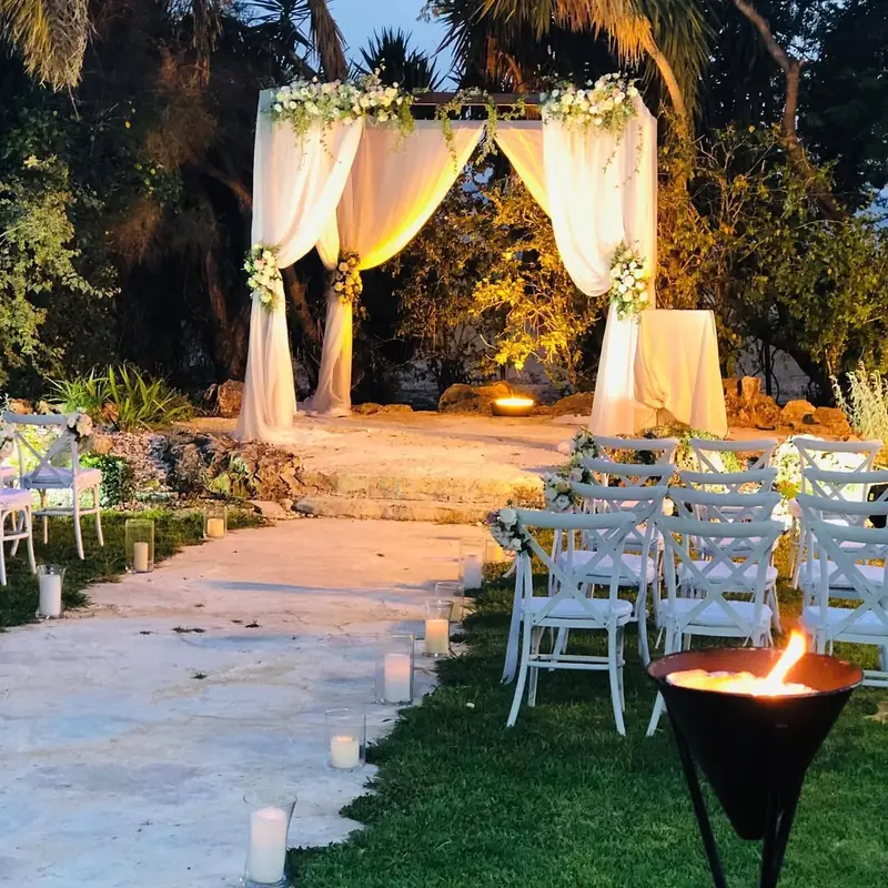 חופה לבנה עם פרחים וכיסאות בגינה לילית